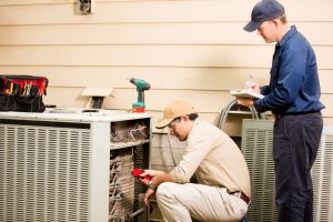 two hvac technicians inspecting the outside unit of an air conditioner