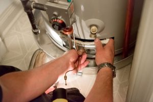 A man uses a flashlight to help him see the boiler in a dark closet